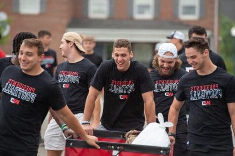 Students with football shirts move in belongings to their residence hall